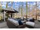 Outdoor patio with wicker furniture seating around a stone-paved gazebo in a lush, wooded backyard at 6170 Wellington Ct, Cumming, GA 30040