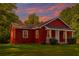 Charming red cottage with a cozy front porch and a well-maintained lawn surrounded by lush trees at 7880 Rivertown Rd, Atlanta, GA 30213