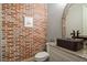 Modern powder room featuring a brick accent wall, vessel sink, and stylish fixtures and mirror at 4465 Newhall Dr, Cumming, GA 30040