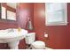 A compact powder room features a pedestal sink, toilet, and a framed mirror, all set against a red wall at 1421 Eryn Cir, Suwanee, GA 30024