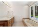 Bathroom with large vanity mirror, double sinks, bathtub, and a view overlooking the yard at 6475 Holland Dr, Cumming, GA 30041