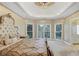 Luxury primary bedroom with decorative headboard, tray ceiling, chandelier, and large windows offering serene outdoor views at 910 Renaissance Way, Roswell, GA 30076