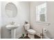 Cozy half bathroom featuring pedestal sink, round mirror, toilet, wood-look floors, and natural light from the window at 2808 Blandwood Rd, Marietta, GA 30064