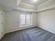 Neutral carpeted bedroom showcasing tray ceiling and natural light from a large window at 3348 Terrace Hedge Pl, Dacula, GA 30019