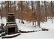 Stone outdoor fireplace with a snow-covered backyard and wooded backdrop at 9625 River Lake Dr, Roswell, GA 30075