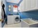 Laundry room with blue walls features a washer, dryer, utility sink, and upper cabinets at 4543 Fairecroft Ter, Suwanee, GA 30024