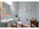 Stylish powder room with pedestal sink, light blue walls, framed art and wood-look flooring at 8220 Majors Ridge Way, Cumming, GA 30041