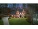 Exterior home view shows a well-lit brick house with a green lawn and side yard at dusk at 4000 Rockingham Dr, Roswell, GA 30075