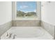 A soaking tub with tiled surround sits beneath a window in the well-lit bathroom at 2023 Wyndham Pl, Conyers, GA 30013