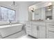 Bright bathroom featuring a soaking tub under an ornate window and vanity with drawers at 7015 Polo Dr, Cumming, GA 30040