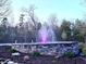 An opulent stone fountain is surrounded by a beautiful flower bed with a lush wooded landscape in the background at 2150 Fincher Rd, Canton, GA 30114