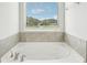 Large soaking tub with tile surround and a view outside the window at 2027 Wyndham Pl, Conyers, GA 30013