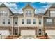 Attractive townhome featuring neutral siding, stone accents, individual garages, and a charming balcony under a partly cloudy sky at 2020 Manor Pointe Dr, Cumming, GA 30041