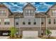 Townhome exterior with neutral siding, stone accents, individual garages, and mature landscaping under a partly cloudy sky at 2020 Manor Pointe Dr, Cumming, GA 30041