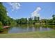 Scenic pond with a dock and fountain, surrounded by lush trees and a clear blue sky at 3195 Ne Wills Mill Ne Rd, Cumming, GA 30041