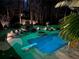 Nighttime view of a backyard pool with diving board, a hot tub, stone fireplace, and lounge seating at 3045 Camp Branch Rd, Buford, GA 30519