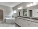 Bright bathroom with dual sinks, corner tub, gray tiled flooring and a door to an additional space at 607 Leland Pkwy, Cumming, GA 30041
