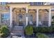 Charming brick front porch with seating, columns, brick steps, manicured shrubs, and black iron railings at 4590 Gablestone Xing, Hoschton, GA 30548