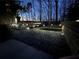 Illuminated backyard with landscape lighting, featuring a deck, stone retaining wall, and mature trees at 650 Vinings Estates Se Dr, Mableton, GA 30126