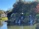 Scenic view of a multi-tiered rock waterfall flowing into a peaceful pond with lush greenery at 6000 E Andechs Smt, Johns Creek, GA 30097