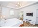Bright main bedroom featuring a tray ceiling, modern light fixture, and French doors leading to the ensuite bathroom at 5730 Paces Pl, Suwanee, GA 30024