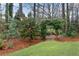 Close up of landscaping featuring a flower bed with green shrubbery and a mature tree with dark red flowers at 1900 Sanborne Way, Dacula, GA 30019