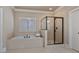Bathroom featuring a tiled tub, a glass shower with a black frame, and neutral tile flooring at 13029 Dartmore Ave, Alpharetta, GA 30005