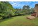 Backyard with trees, shrubbery, lush green lawn, and a gravel area beside the house at 12040 Old Mountain Park Rd, Roswell, GA 30075