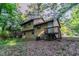 Angled view of the rear of the two-story home surrounded by mature trees, grass and a small wooden deck at 4342 Lincolndale Dr, Ellenwood, GA 30294