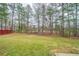 Spacious backyard with mature trees and an unkept lawn with a red fence at the border at 104 Shadow Creek Ct, Fairburn, GA 30213