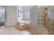 Bright bathroom featuring a glass block shower, soaking tub with tile surround, and neutral tile flooring at 1617 Windsor Ne Pkwy, Brookhaven, GA 30319