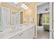 Bright bathroom featuring double sinks, a large mirror with vanity lighting, and view into bedroom at 6350 Bridge Brook Ovlk, Cumming, GA 30028