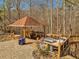 Outdoor gazebo with a grill, seating area, and wood flooring, surrounded by a stone patio and mature trees at 3460 Mansions Pkwy, Berkeley Lake, GA 30096