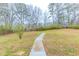 View of the grassy backyard and a concrete walkway with bare trees in the background at 6202 Humphries Hill Rd, Austell, GA 30106