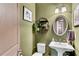 Stylish powder room with a pedestal sink, oval mirror, and sage green walls at 2318 Willington Shoals Se Pl, Smyrna, GA 30080