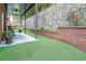 Landscaped backyard with a covered patio, artificial turf, a stone retaining wall, and lush greenery at 3280 Stillhouse Se Ln # 108, Atlanta, GA 30339