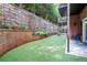 Manicured backyard with artificial turf, retaining wall with plants, and a covered patio with nearby brick building at 3280 Stillhouse Se Ln # 108, Atlanta, GA 30339