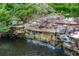 Stone-lined water feature with a small cascading waterfall in a wooded setting at 203 Glenrise Ct, Woodstock, GA 30188