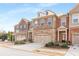View of townhome exteriors featuring brick facades, attached garages, and manicured landscaping under a blue sky at 2286 Emerald Sky Dr, Smyrna, GA 30080