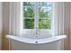 Bright bathroom featuring a soaking tub, white tile, and a large window overlooking lush greenery at 4975 Rebel Trl, Atlanta, GA 30327