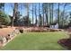 Backyard featuring an artificial turf lawn, a rock retaining wall, and various trees at 5569 Snowy Orchid Dr, Sugar Hill, GA 30518