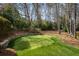 Backyard putting green with stone retaining wall and mature trees offering a private golf practice area at 3180 Wills Mill Rd, Cumming, GA 30041