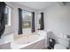 Bathroom with a white soaking tub next to windows, toilet, and marble countertops at 331 Cobblestone Rd, Auburn, GA 30011