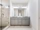 Bright bathroom featuring a granite countertop, double sinks, a large mirror, and a glass-enclosed shower with marble tile at 6145 Stargazer Way, Cumming, GA 30028
