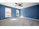 This bedroom features blue walls, gray carpet, a ceiling fan, and two windows that provide natural light and neighborhood views at 3290 Coachmans Ne Way, Roswell, GA 30075