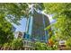 Modern high-rise building featuring blue glass exterior and multiple balconies, seen through lush green trees at 1080 Peachtree Ne St # 2309, Atlanta, GA 30309