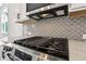 Close-up of a stainless steel gas range with a stylish gray tile backsplash and white cabinets at 1696 Gunnin Nw Trce # 244, Atlanta, GA 30318