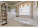 The main bathroom featuring a large soaking tub with tile surround and a window with privacy blinds at 4780 Woodruff Trce, Cumming, GA 30028