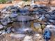 Close-up of a backyard waterfall featuring mossy rocks and whimsical figurines at 3304 Woolbridge Ct, Marietta, GA 30062
