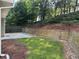 Landscaped backyard featuring green grass, concrete patio, wood retaining wall, and lush trees beyond at 1558 Autumn Wood Trl, Sugar Hill, GA 30518